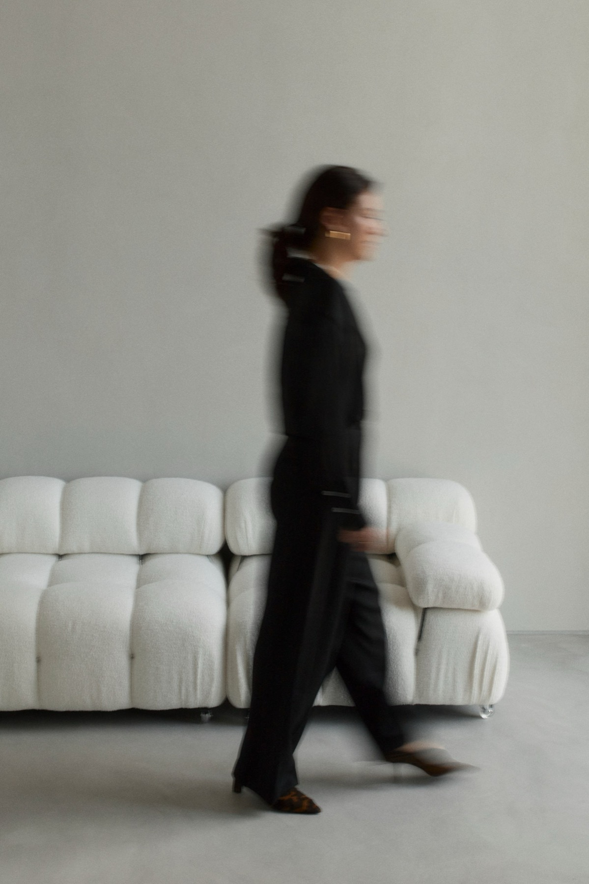 Ksenia in black, walking past a white sofa, in motion